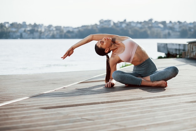 Young woman with slim type of body does exercises against lake