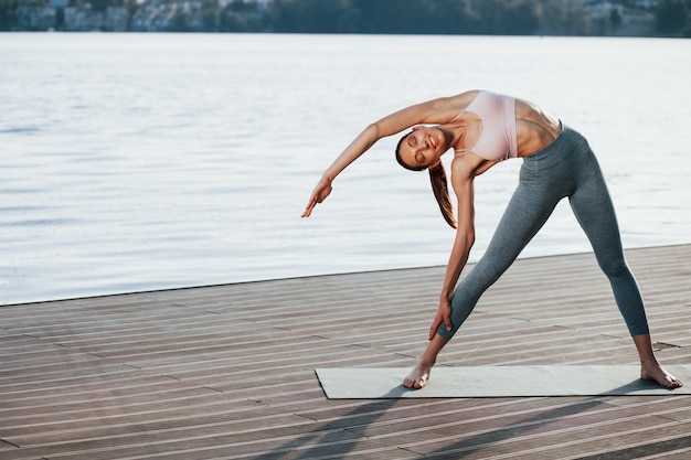 Young woman with slim type of body does exercises against lake