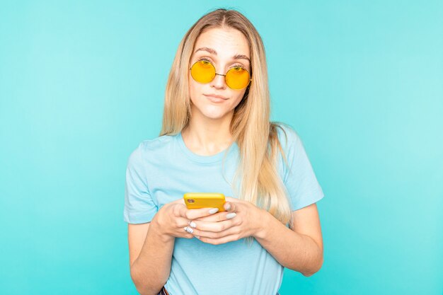 Photo young woman with smartphone over isolated blue surprised and sending a message.