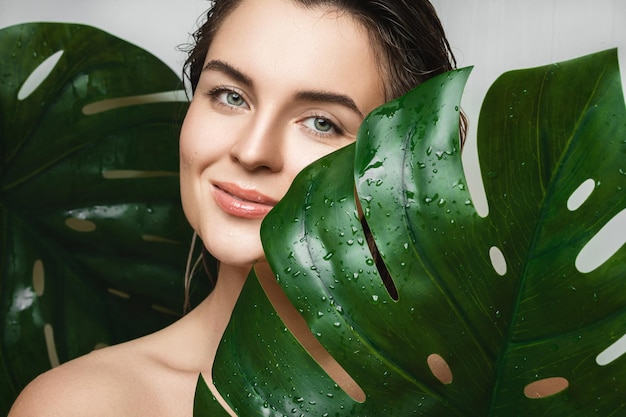 Young woman with a smooth skin holding Monstera deliciosa plant leaf