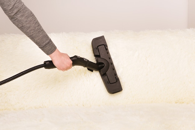 Young woman with a steam cleaner cleans the carpet on the couch