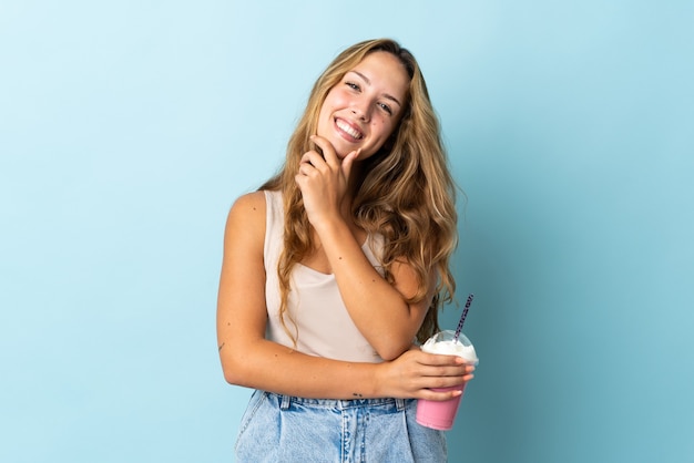 Young woman with strawberry milkshake isolated on blue wall happy and smiling