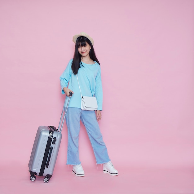 Young woman with suitcase on pink wall