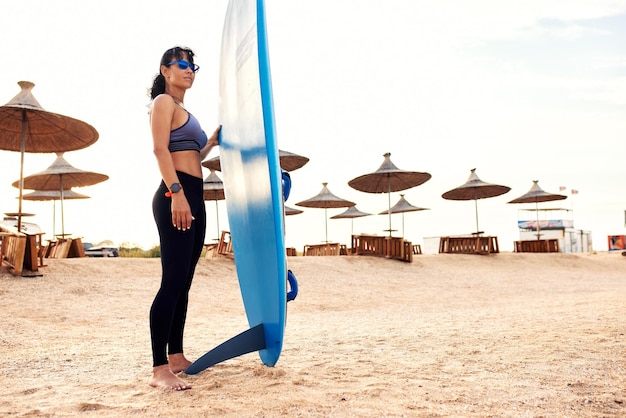 Young woman with a surf stands on the beach waiting for a ride