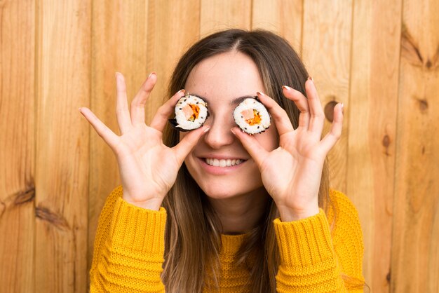 Young woman with sushi over wood wall