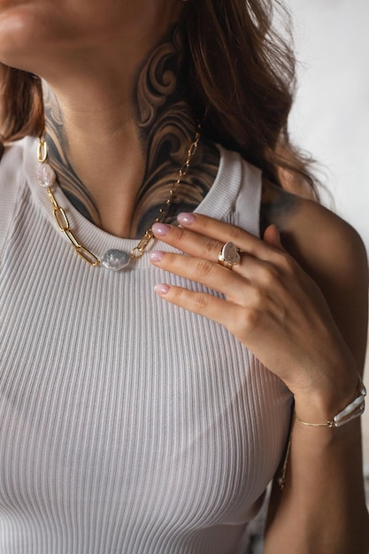 Photo young woman with a tattoo shows off jewelry on her neck and arm a necklace with pearls and a ring