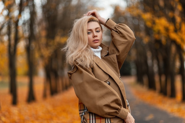 Photo young woman with a trendy hairstyle in an elegant coat poses outdoors in a park