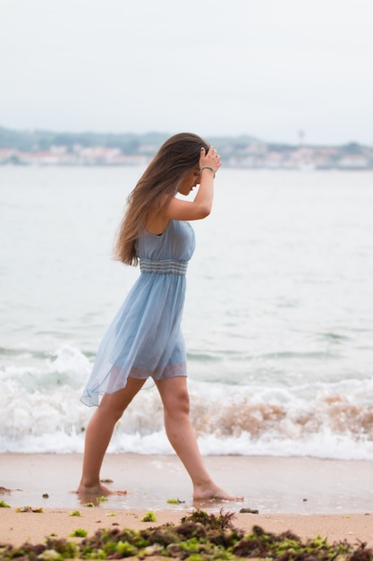 Young woman with a turquoise dress walking through the beach