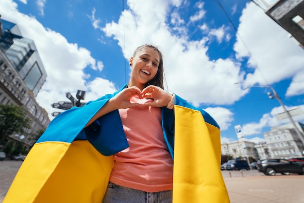 Young woman with Ukrainian flag shows heart with hands