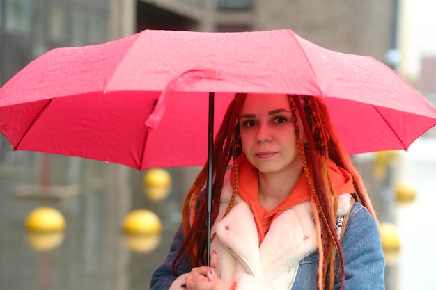 Young woman with umbrella on street Positive young female in warm clothes smiling while standing on city street