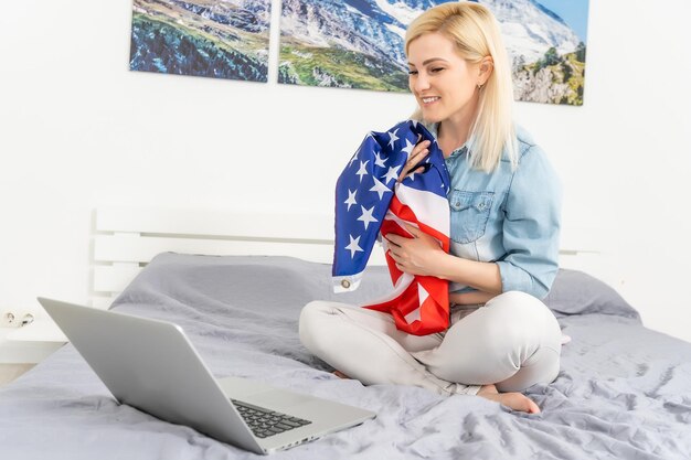 Young woman with USA flag using a laptop computer, independence day online.