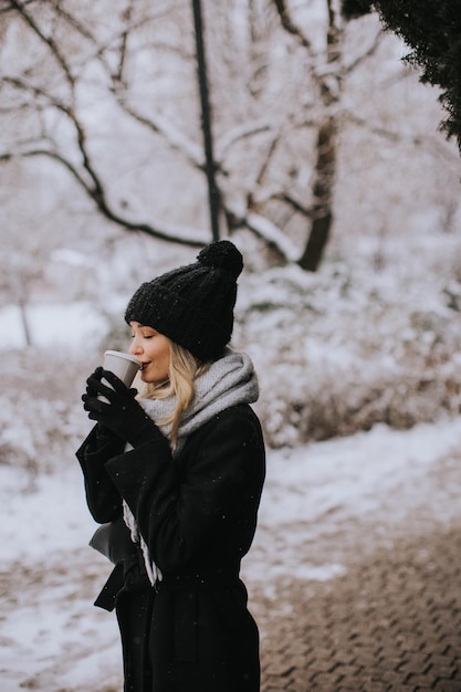 Young woman with Warm Clothes in Cold Winter Snow drinking coffee to go