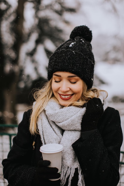 Young woman with Warm Clothes in Cold Winter Snow drinking coffee to go