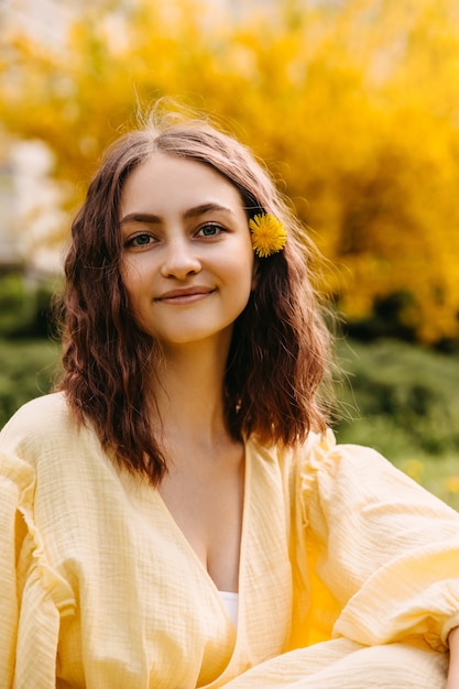 Young woman with wavy hair sitting in a garden with a dandelion in her hair smiling