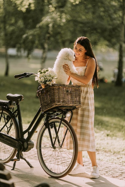 Young woman with white bichon frise dog in the basket of electric bike