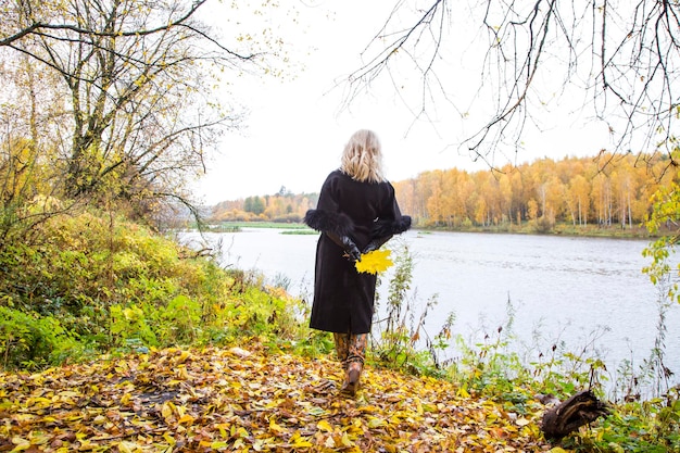 Young woman with yellow leaves walking outside in autumn park