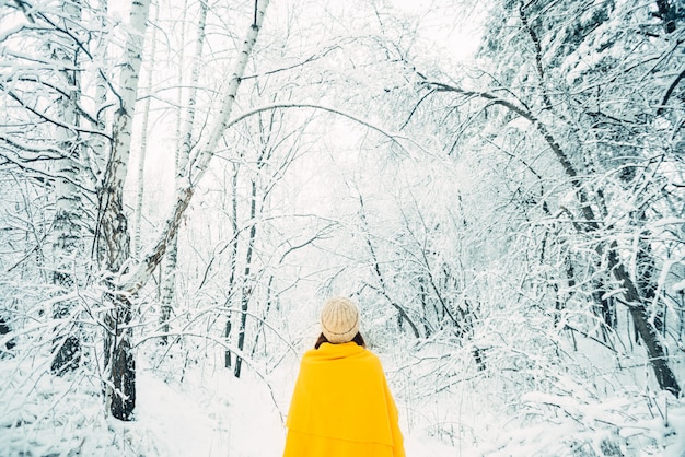 Young woman with a yellow plaid in a snowy forest, rear view. Winter mood.