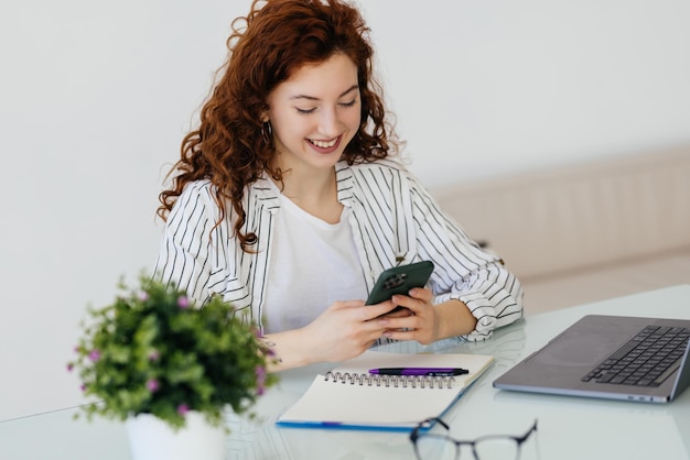 Young woman worker sitting on the workdesk and using cellphone