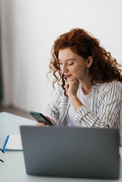 Young woman worker sitting on the workdesk and using cellphone