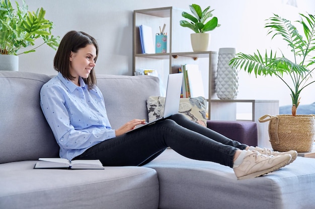 Young woman working from home using laptop making notes