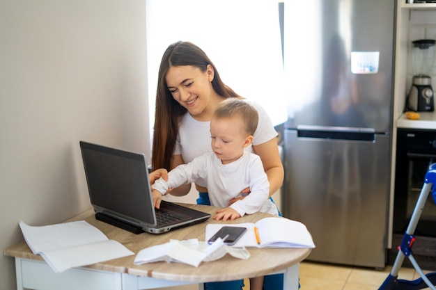 Young woman working at home with a laptop with a baby on his hands