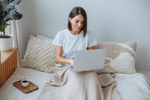 Young woman working on laptop at home in bed