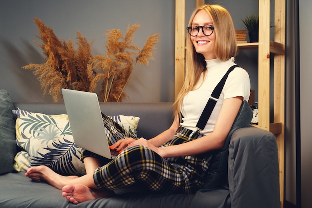 Young woman working on laptop at home, sitting on the sofa