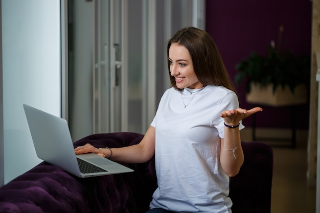 Young woman working on a laptop. Pretty girl using laptop, working at home, relaxing on the couch. Teleworking, teleworking, quarantine, digital nomad, stay at home concept