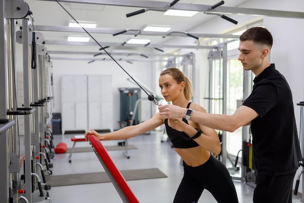 Young woman working with a fitness instructor on a cable weight lifting machine