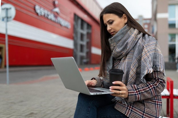 Young woman working with a laptop in her hands next to an office building