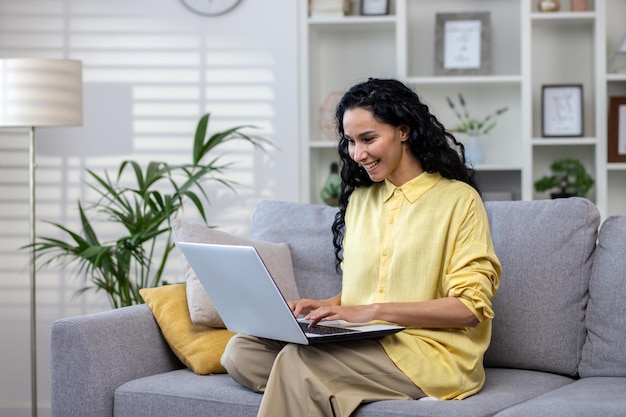 Young woman working with laptop sitting on sofa at home successful latin american woman in living