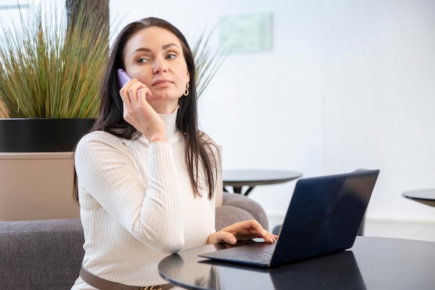 Young woman works on laptop and smartphone in cafe