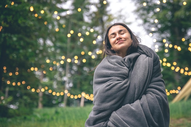 A young woman wrapped in a blanket in the forest on a blurred background