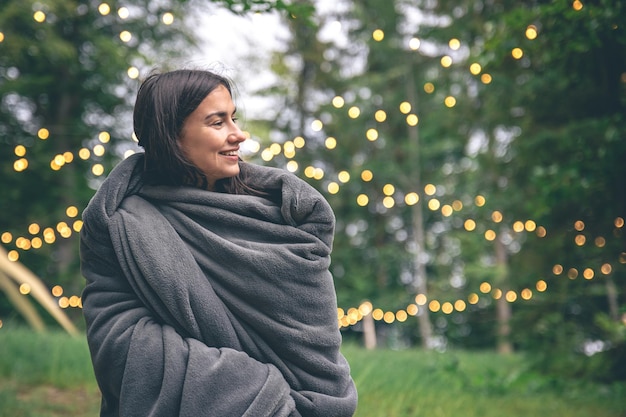 A young woman wrapped in a blanket in the forest on a blurred background