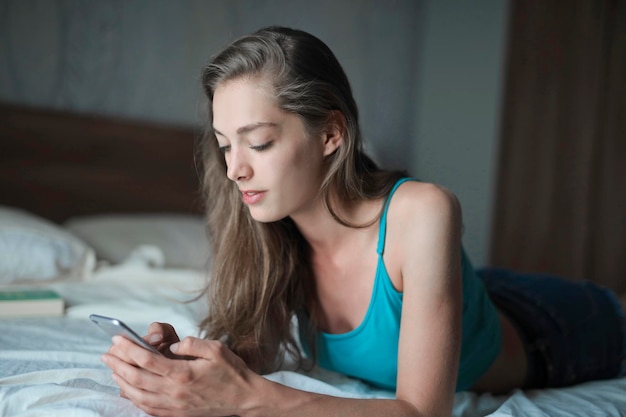 young woman writes with smartphone lying on a bed