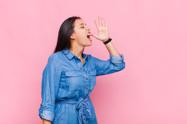 Young woman yelling loudly and angrily to copy space on the side, with hand next to mouth