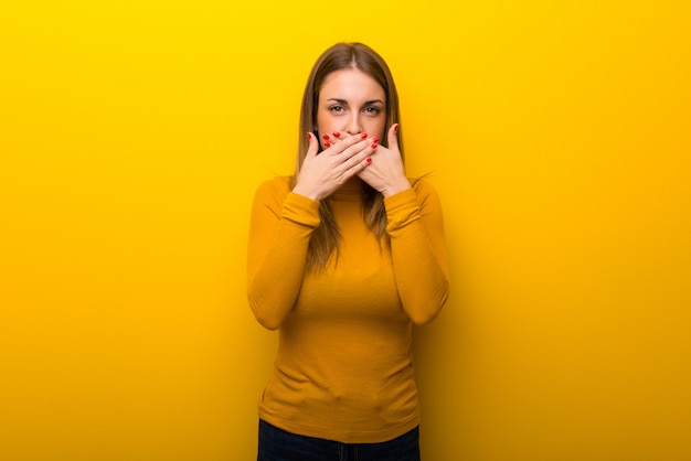 Young woman on yellow background covering mouth with hands for saying something inappropriate