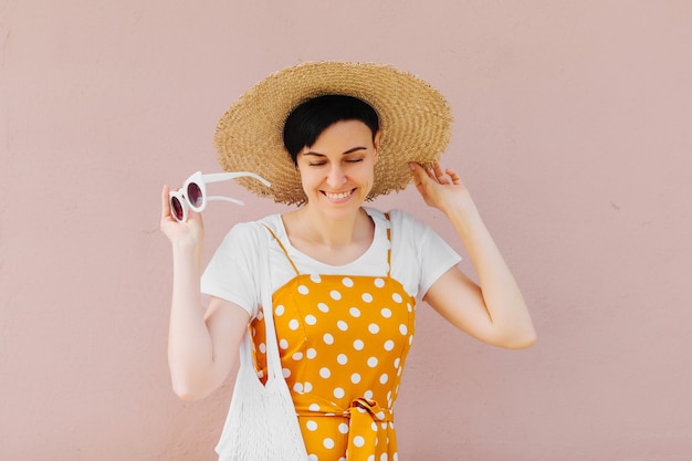 Young woman in yellow clothes and straw hat with sunglasses on light beige background