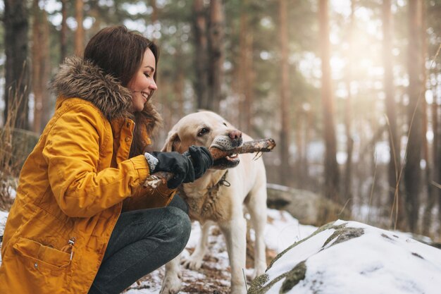 Young woman in yellow jacket trains big kind white dog Labrador walking in the winter forest