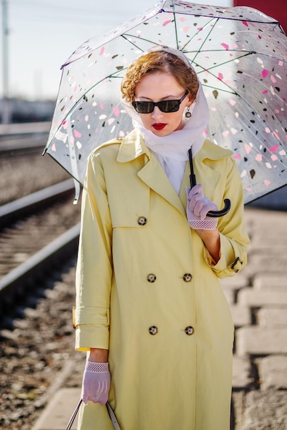 A young woman in yellow raincoat and dark glasses with umbrella in her hands Retro style portrait