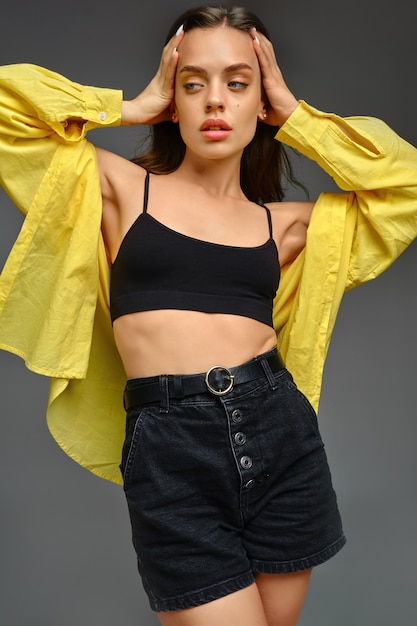 Young woman in yellow shirt posing on grey background