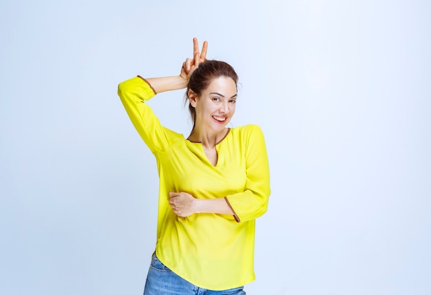 Young woman in yellow shirt showing rabbit ears