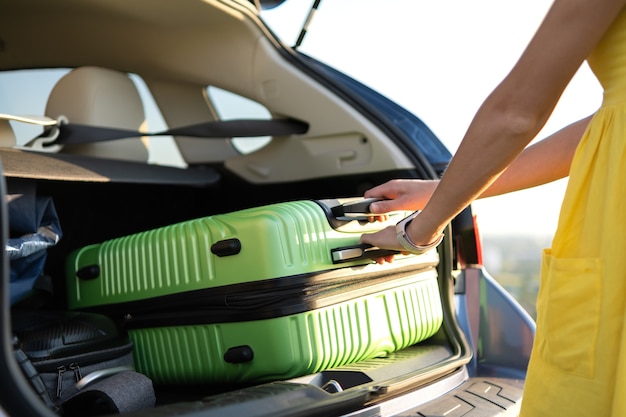 young woman in yellow summer dress taking green suitcase from car trunk