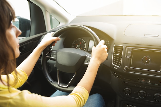 Young woman in yellow sweater and blue jeans holding the steering wheel of a car from inside the cabi