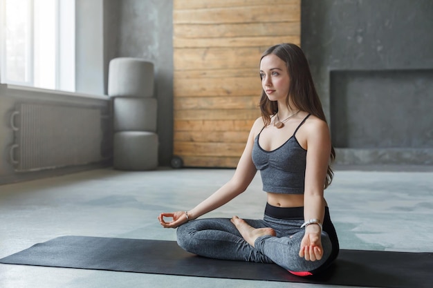 Young woman in yoga class, meditation exercises. Girl does lotus pose for relaxation. Healthy lifestyle in fitness club