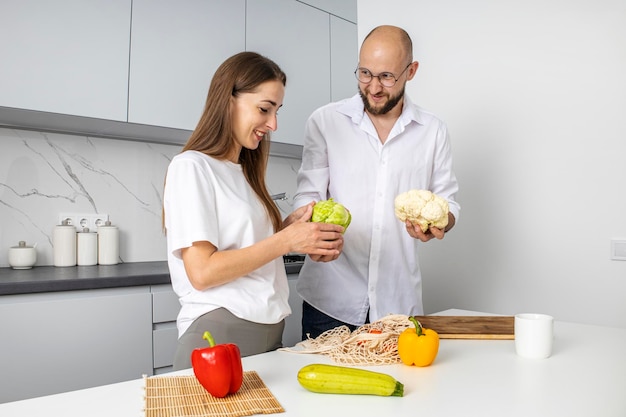 Young woman and young man putting out fresh vegetables from the bag in the kitchen