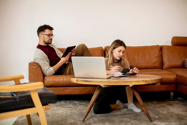 Young woman and young man using laptop while sitting by the sofa at home