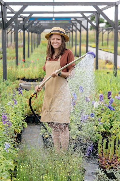 Young womangardener watering garden plants in garden center