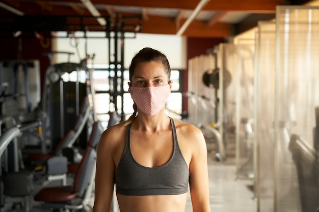 Young womanr with face mask looking at camera in gym.