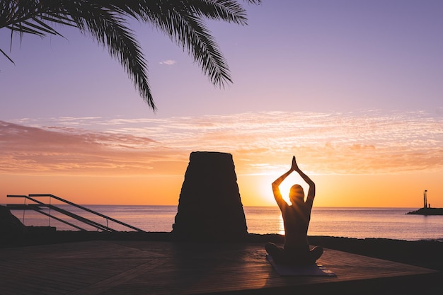 Photo young womans silhouette meditating in front of the beach at sunrise